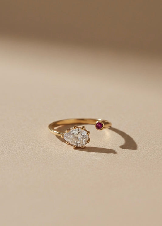 Anillo 27 de tono dorado con piedra transparente en forma de lágrima y detalle redondo granate